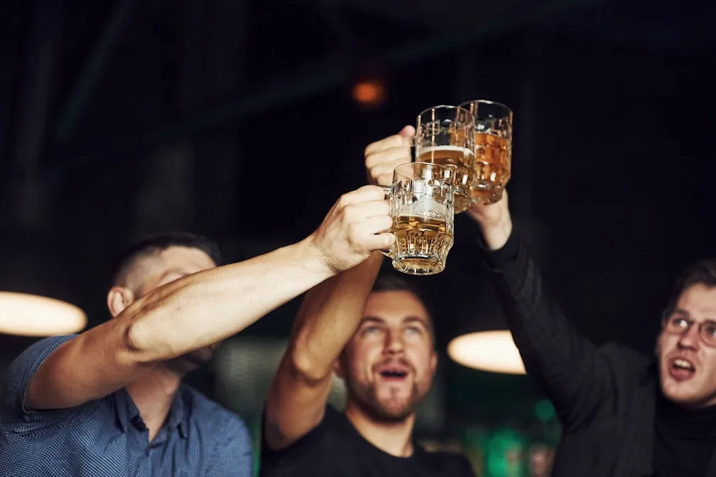 Three friends raising beer mugs in a warmly-lit pub — reference for Dubliner imagery